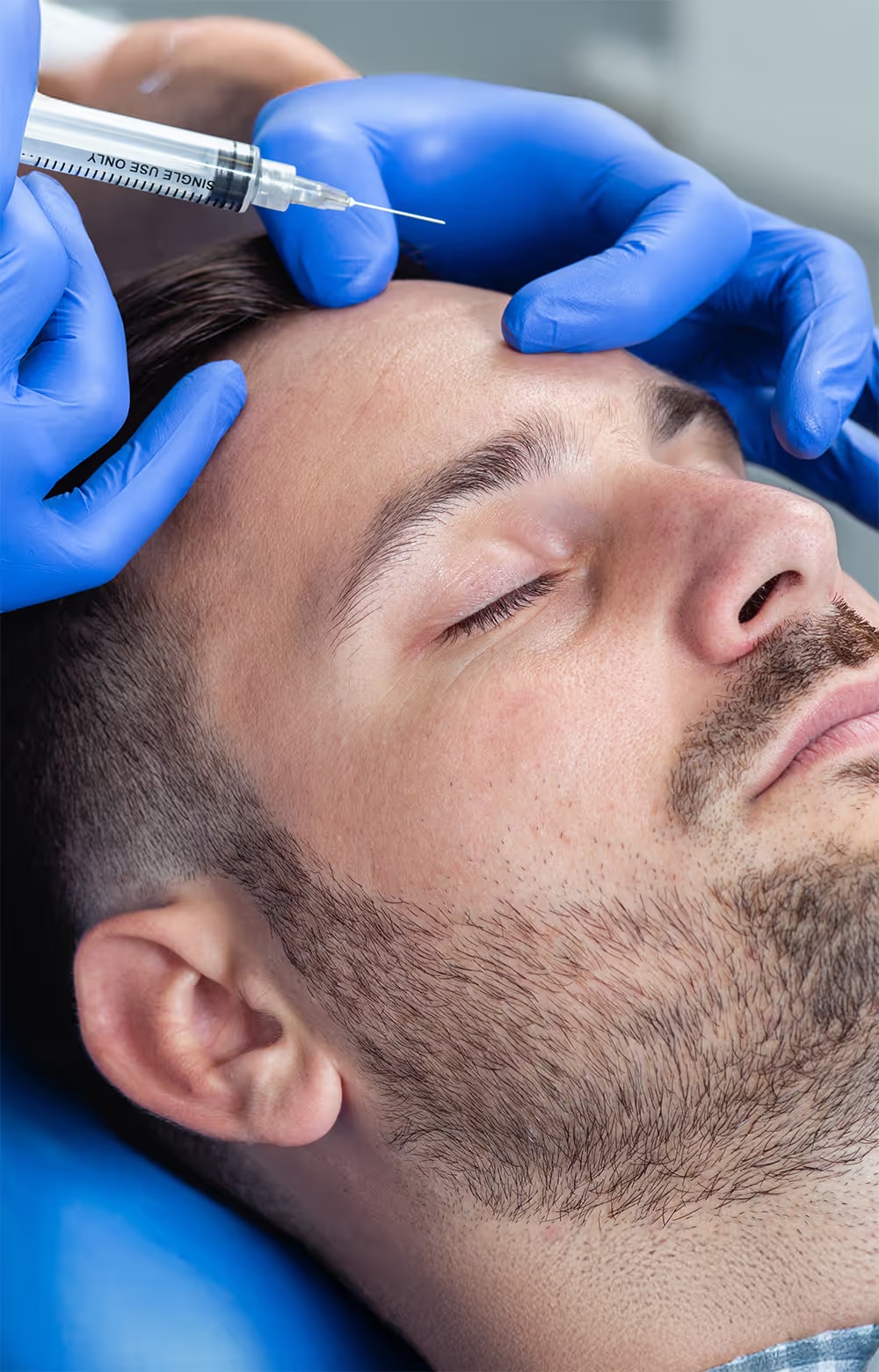 Patient lying down as clinician in blue gloves performs a facial cosmetic procedure.