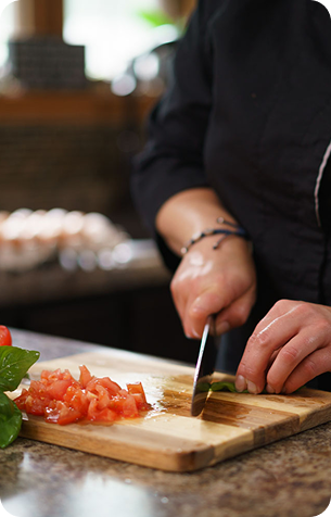 Close-up of a chef's hands dicing fresh tomatoes on a wooden cutting board.