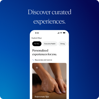 Smartphone mockup on a dark blue background displaying the Explore Mayo screen with personalized experiences and a Rejuvenate Spa card featuring a photograph of a massage. Above the phone, a heading reads “Discover curated experiences.”