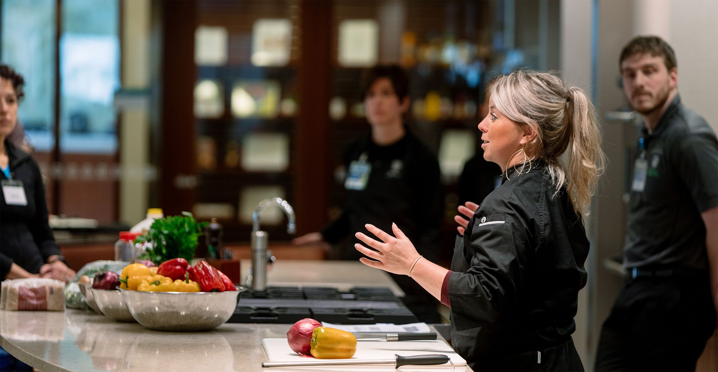 Female chef standing at a kitchen counter having a conversation with Executive Health patients.