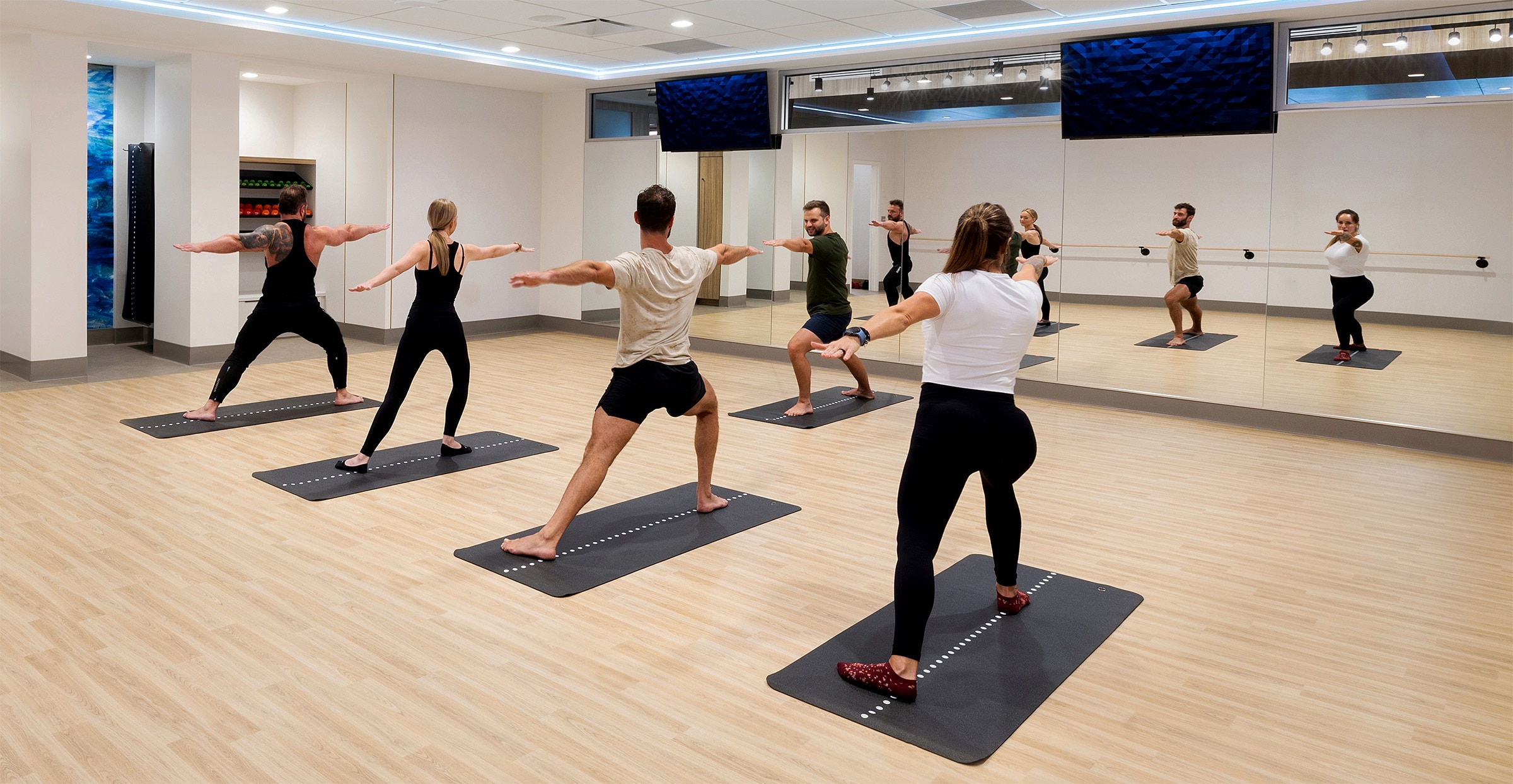 Four individuals being taught yoga by a male instructor in a professional yoga studio environment.