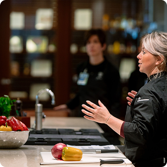 Female chef standing at a kitchen counter having a conversation with Executive Health patients.