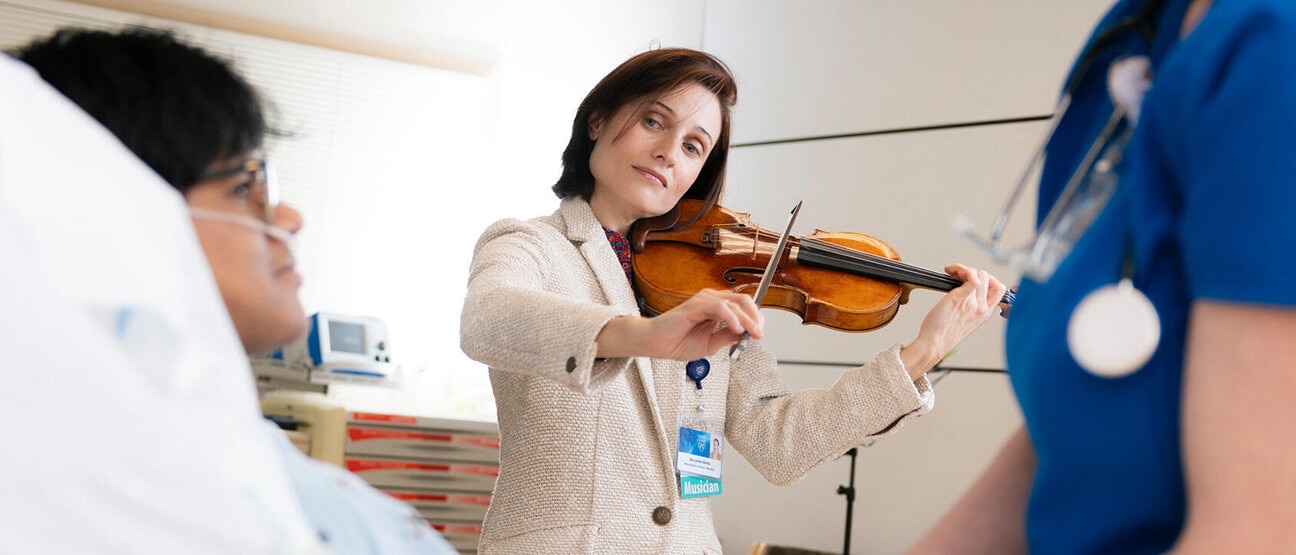 A volunteer plays a violin for a patient in the hospital.