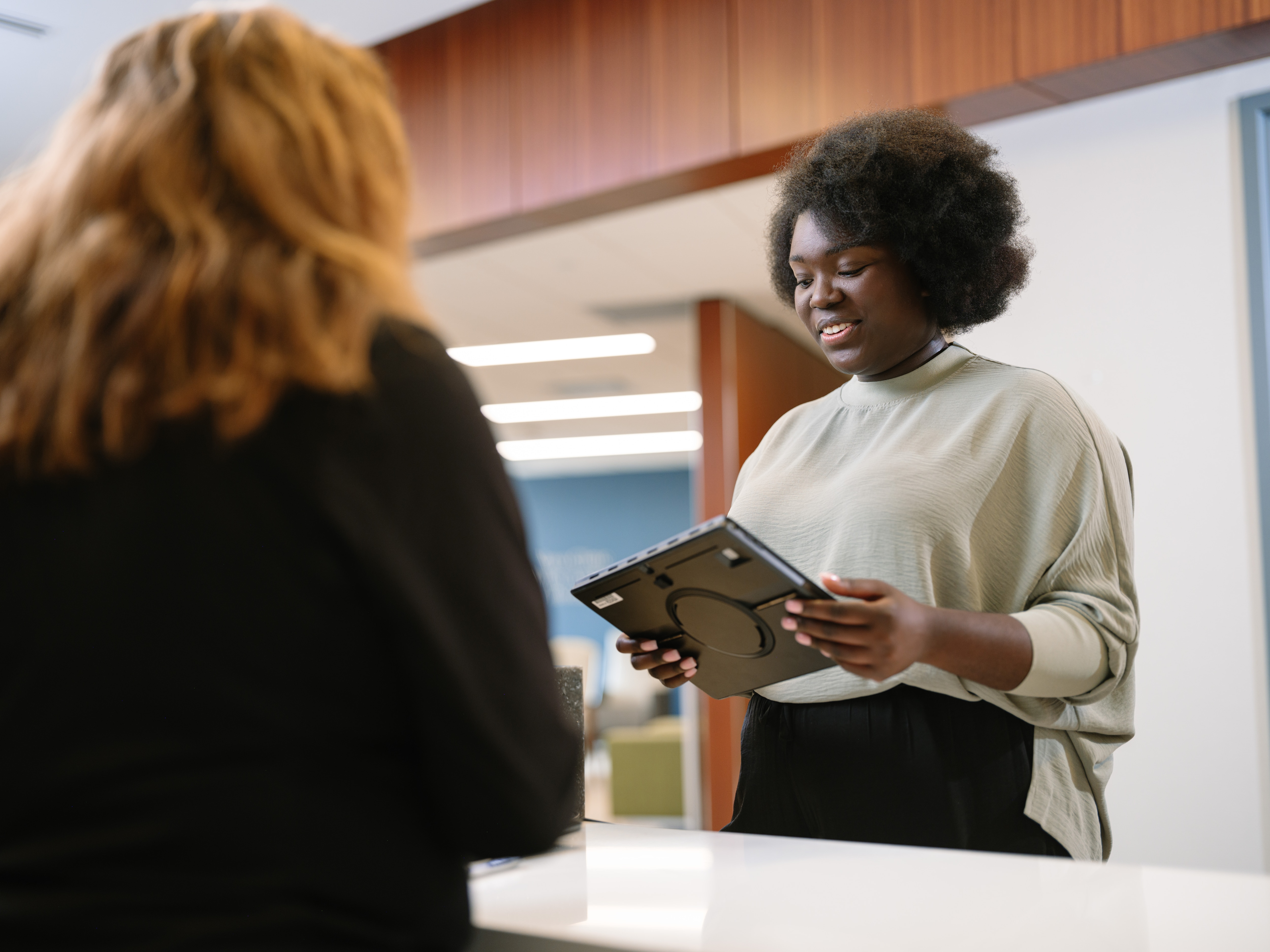 A patient returns a tablet to a staff member at a check-in desk.